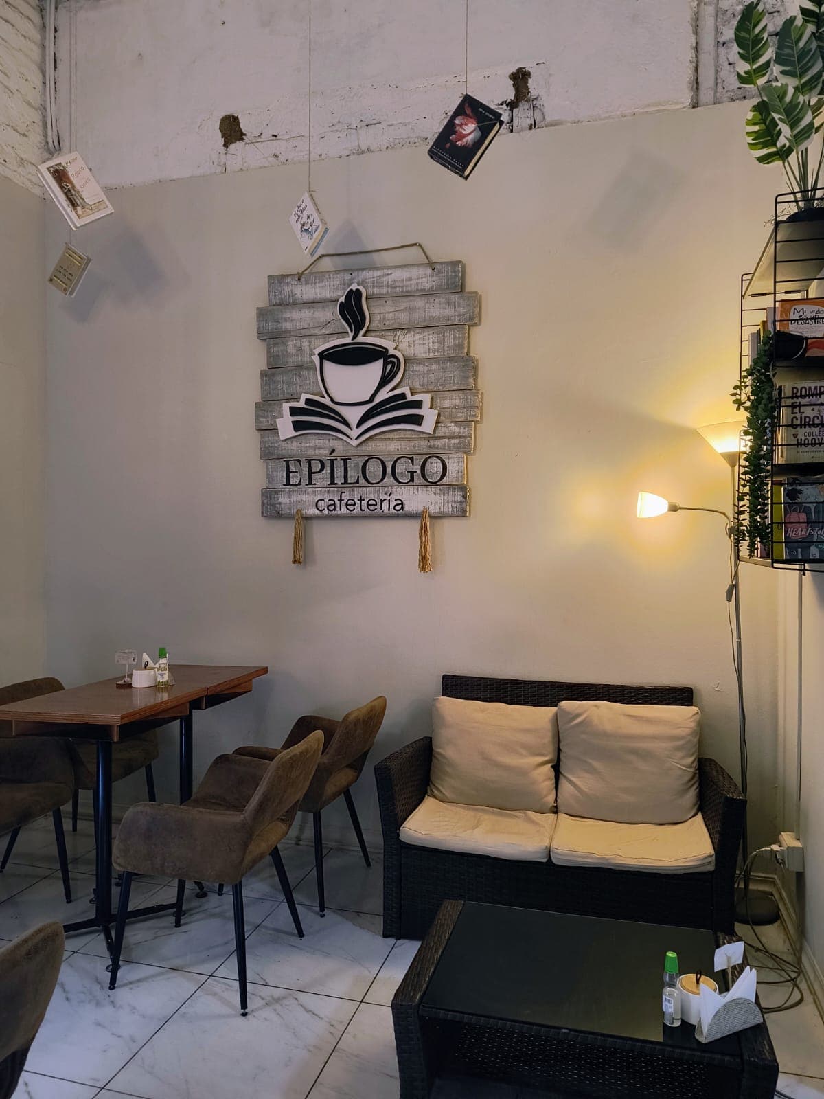 Rincón con sillón y el letrero de Epílogo Cafetería, con libros colgando del techo