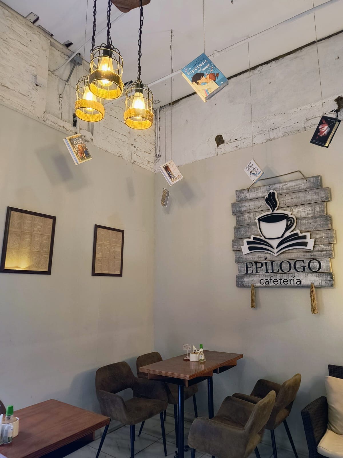 Mesas bajo lámparas de jaula y libros colgantes, junto al letrero del local