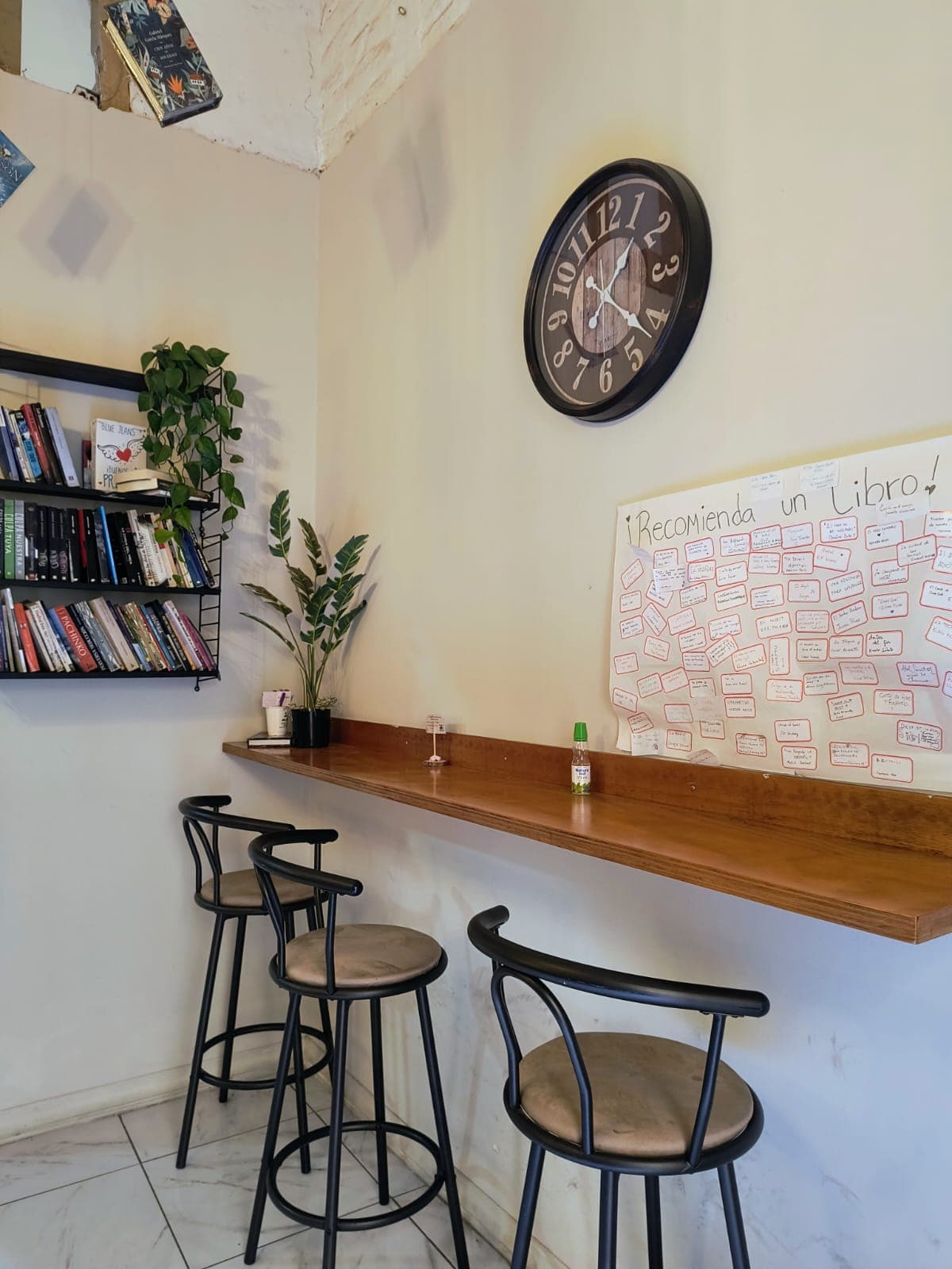 Barra con taburetes, reloj y el mural "¡Recomienda un libro!" de los clientes